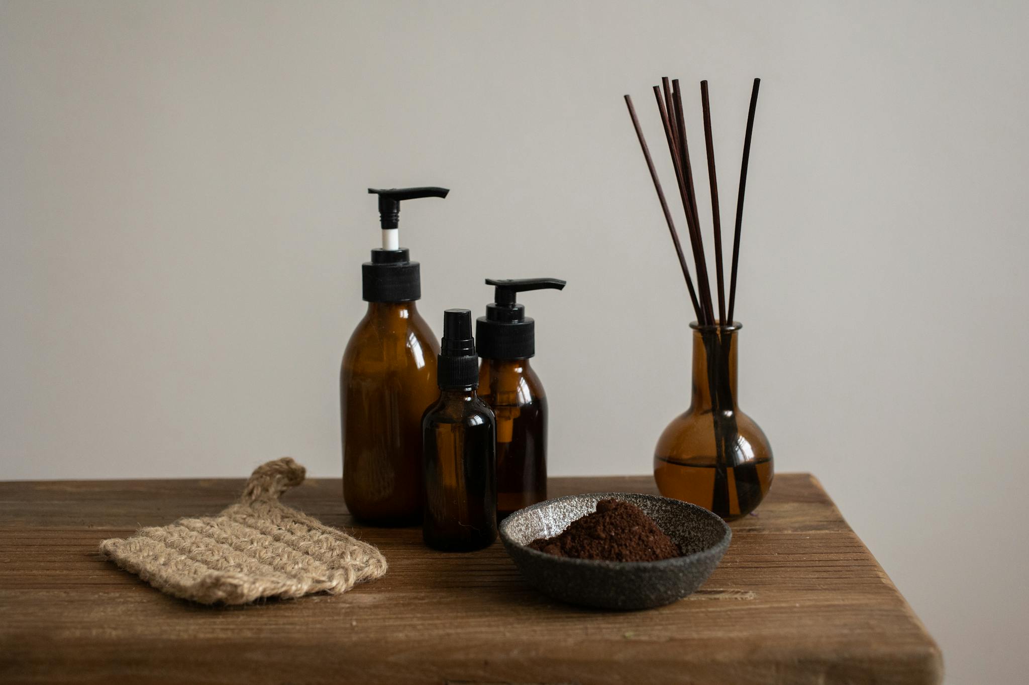 Elegant still life featuring brown bottles with pump dispensers and a reed diffuser on a wooden table.